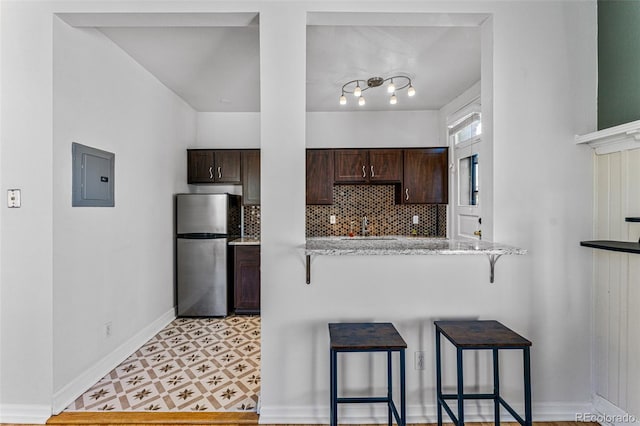 kitchen with electric panel, freestanding refrigerator, dark brown cabinets, a kitchen breakfast bar, and tasteful backsplash