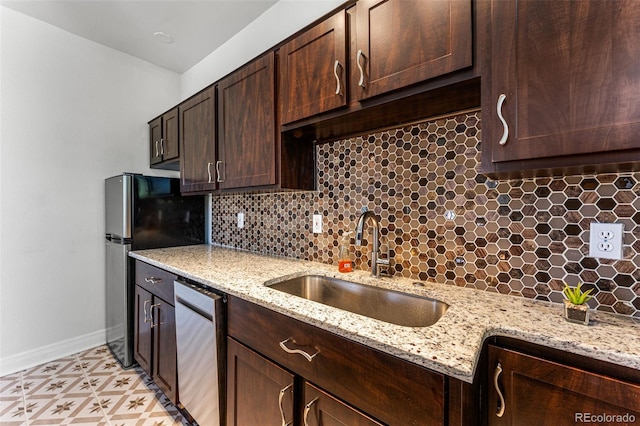 kitchen featuring baseboards, dark brown cabinetry, decorative backsplash, appliances with stainless steel finishes, and a sink