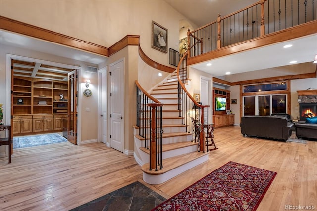 staircase with a high ceiling, built in features, a stone fireplace, and light wood-type flooring