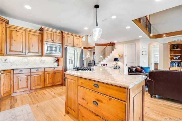 kitchen with decorative light fixtures, light stone counters, stainless steel appliances, light wood-type flooring, and backsplash