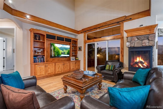 living room featuring a high ceiling, a fireplace, light hardwood / wood-style floors, built in shelves, and plenty of natural light