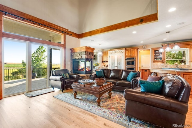 living room featuring a high ceiling, a stone fireplace, sink, and light wood-type flooring