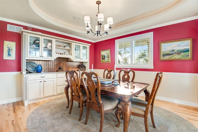 dining space featuring a chandelier, a tray ceiling, ornamental molding, and light hardwood / wood-style floors