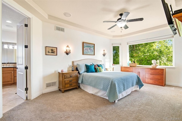 bedroom featuring ceiling fan, sink, light carpet, a raised ceiling, and ensuite bathroom