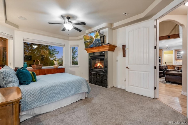 bedroom with ceiling fan, a tile fireplace, and light hardwood / wood-style flooring