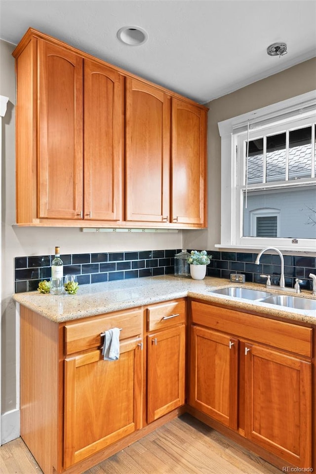 2271 Holly St, Denver, CO 80207 - kitchen with a sink, light wood finished floors, decorative backsplash, light stone counters, and brown cabinetry