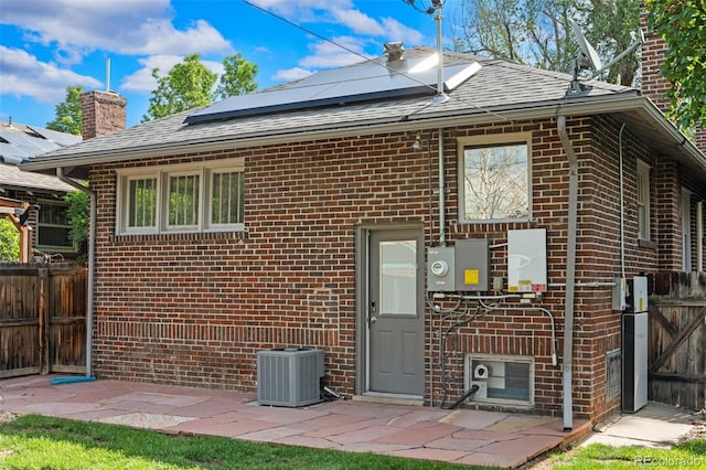 2271 Holly St, Denver, CO 80207 - back of house featuring brick siding, central AC, roof mounted solar panels, a chimney, and roof with shingles
