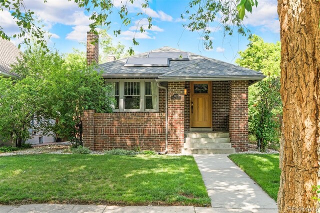 2271 Holly St, Denver, CO 80207 - bungalow-style home with a chimney, roof mounted solar panels, brick siding, a front yard, and a shingled roof