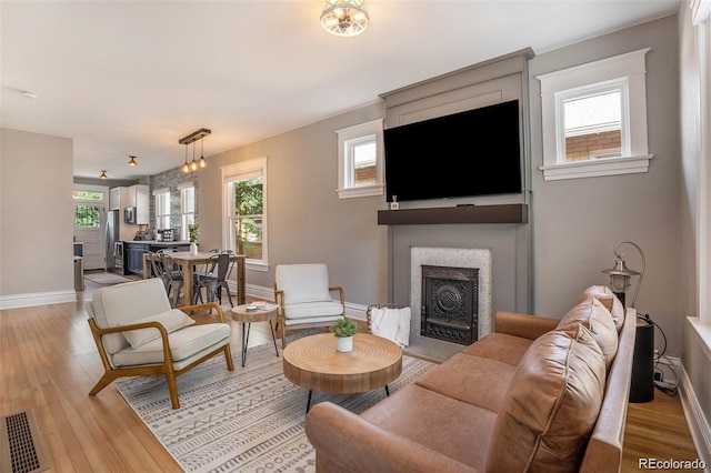 living room with baseboards, light wood-style floors, visible vents, and a large fireplace