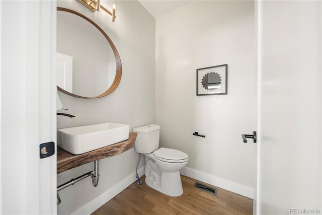 bathroom featuring visible vents, baseboards, a sink, toilet, and wood finished floors