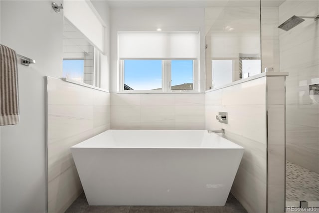bathroom with tile walls, a walk in shower, and a freestanding tub