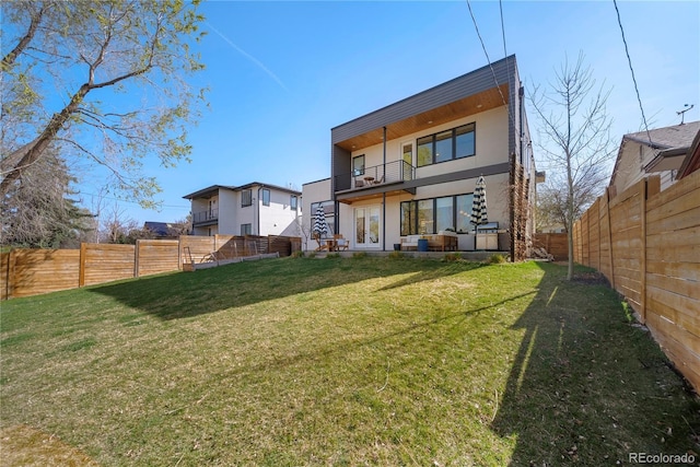 back of house with french doors, a fenced backyard, a yard, and a balcony