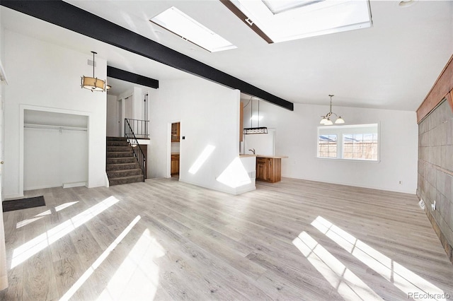 unfurnished living room with a notable chandelier, lofted ceiling with beams, and light wood-type flooring