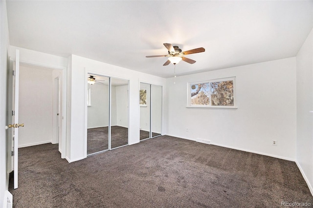 unfurnished bedroom with ceiling fan, dark carpet, and two closets