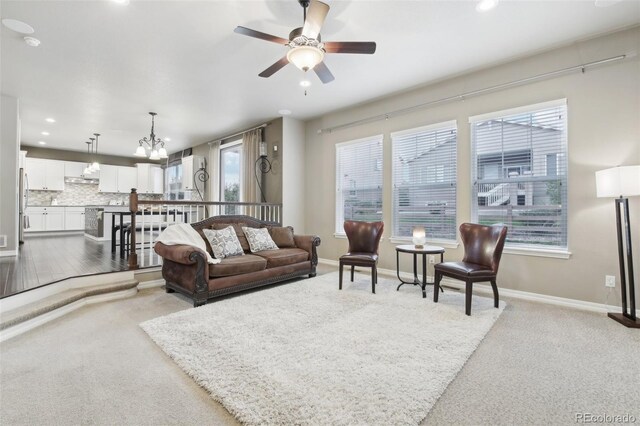 carpeted living room with ceiling fan with notable chandelier