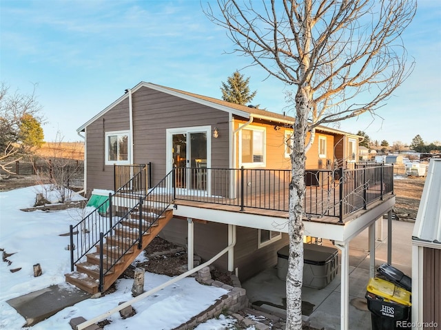 snow covered house featuring a wooden deck and a hot tub