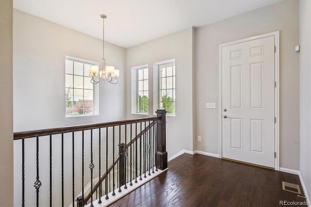 entryway featuring dark wood-style flooring, baseboards, visible vents, and an inviting chandelier