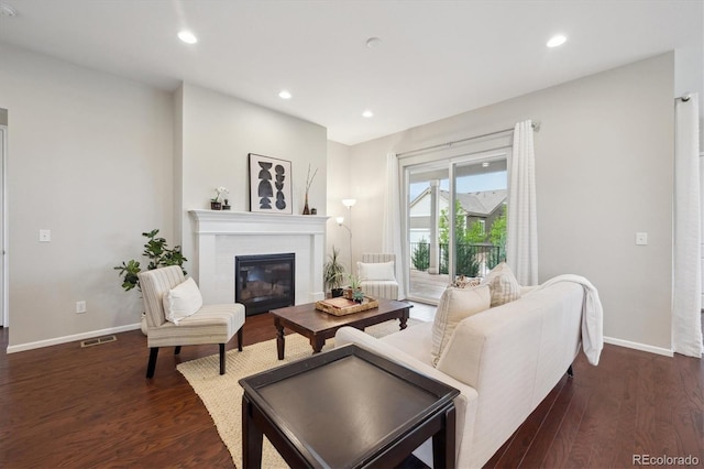 living room featuring a glass covered fireplace, baseboards, dark wood-style floors, and visible vents