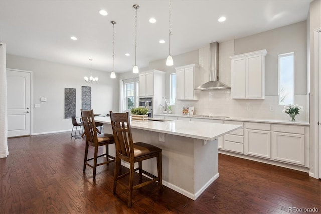 kitchen with wall chimney range hood, oven, light countertops, tasteful backsplash, and a center island with sink