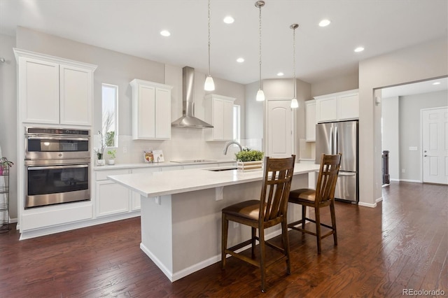 kitchen with appliances with stainless steel finishes, a center island with sink, a sink, recessed lighting, and wall chimney exhaust hood