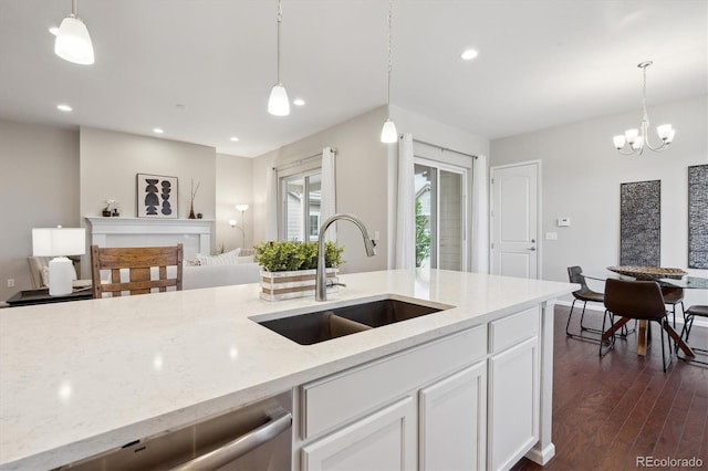 kitchen with dark wood-style flooring, pendant lighting, stainless steel dishwasher, light stone countertops, and a sink
