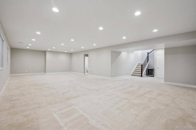 finished below grade area featuring baseboards, stairs, and light carpet