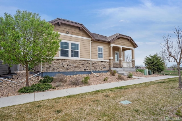 craftsman house featuring a porch, a front yard, and stone siding