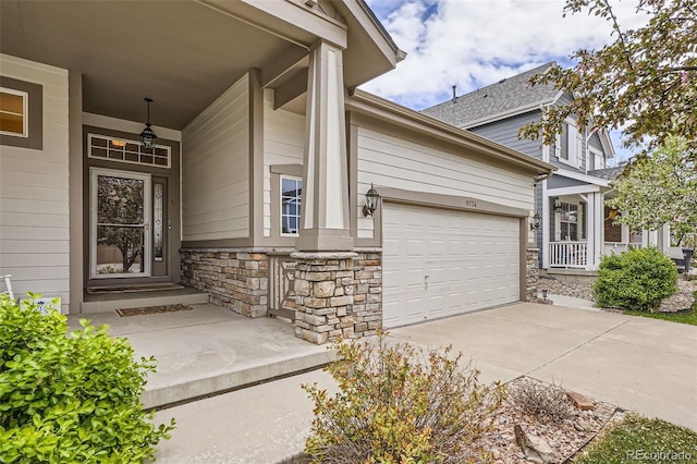entrance to property featuring stone siding, concrete driveway, a porch, and a garage