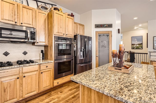 kitchen featuring stainless steel appliances, light wood-style flooring, backsplash, light stone counters, and light brown cabinets