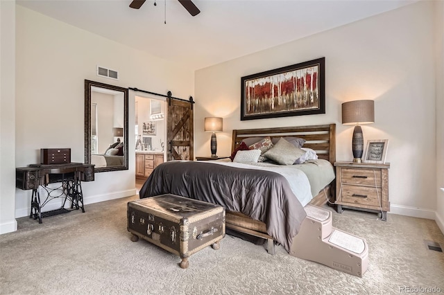 carpeted bedroom with a barn door, baseboards, ensuite bath, and ceiling fan