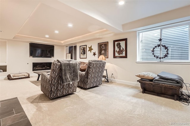 carpeted home theater featuring a tray ceiling, recessed lighting, baseboards, and a glass covered fireplace