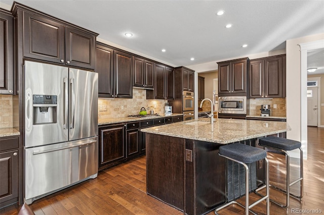 kitchen with dark wood finished floors, appliances with stainless steel finishes, a breakfast bar, dark brown cabinets, and a sink