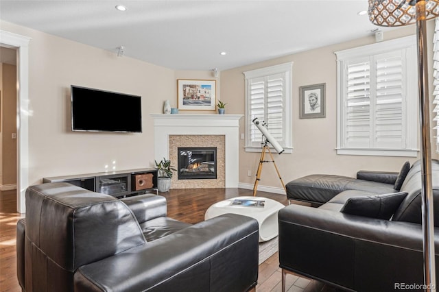 living area with a glass covered fireplace, baseboards, recessed lighting, and wood finished floors