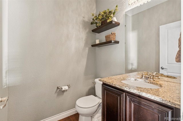 half bath with toilet, baseboards, wood finished floors, and vanity