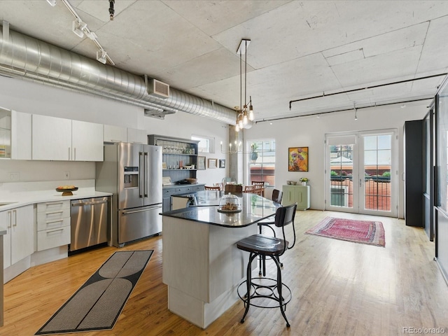 1499 Blake St Unit 3U, Denver, CO 80202 - kitchen with appliances with stainless steel finishes, light wood-style flooring, a kitchen breakfast bar, white cabinetry, and a kitchen island
