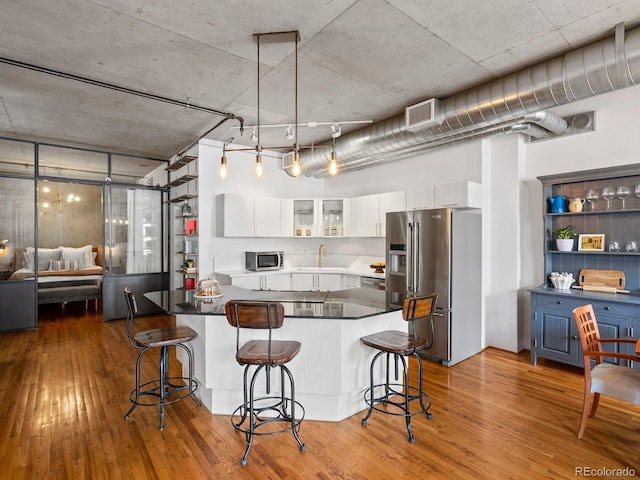 1499 Blake St Unit 3U, Denver, CO 80202 - kitchen with stainless steel appliances, white cabinets, a breakfast bar, hardwood / wood-style flooring, and glass insert cabinets