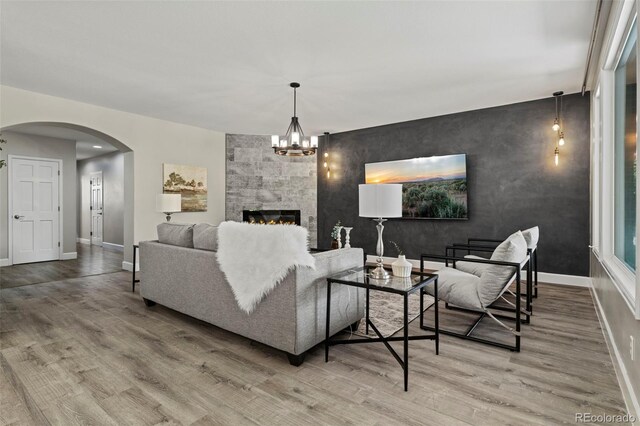 7119 S Riviera St, Aurora, CO 80016 - living area featuring wood finished floors, an accent wall, arched walkways, a fireplace, and a chandelier