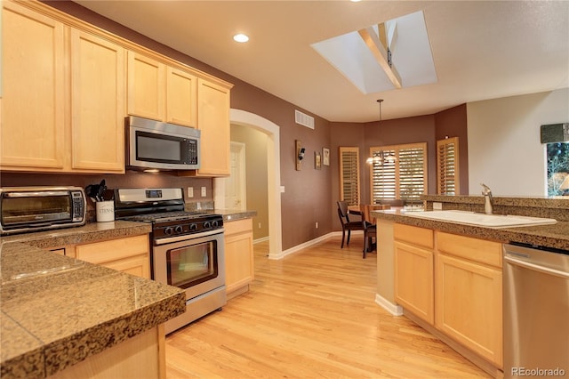 kitchen featuring a skylight, sink, stainless steel appliances, pendant lighting, and light hardwood / wood-style floors