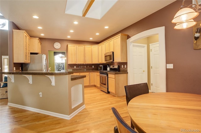 kitchen with light hardwood / wood-style flooring, light brown cabinetry, appliances with stainless steel finishes, kitchen peninsula, and a breakfast bar area