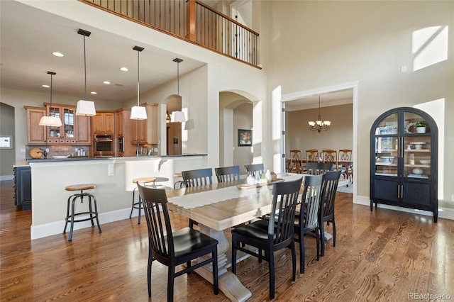 dining room with a notable chandelier, dark wood-type flooring, a wealth of natural light, and a high ceiling