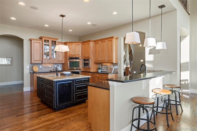 kitchen featuring tasteful backsplash, hanging light fixtures, double oven, and an island with sink