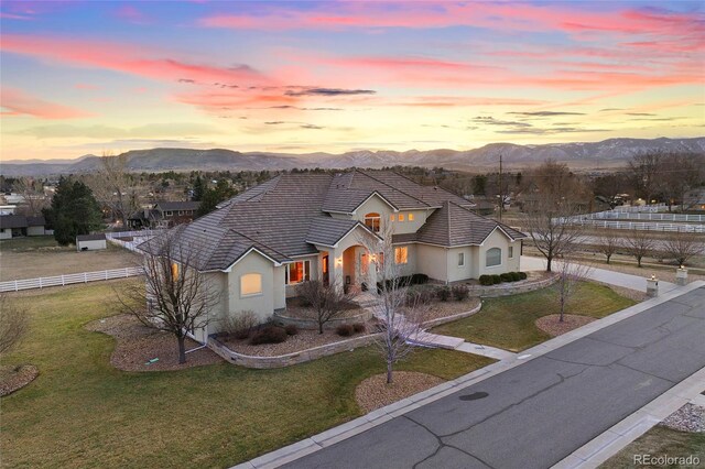 traditional-style home featuring a mountain view, stucco siding, fence, and a lawn