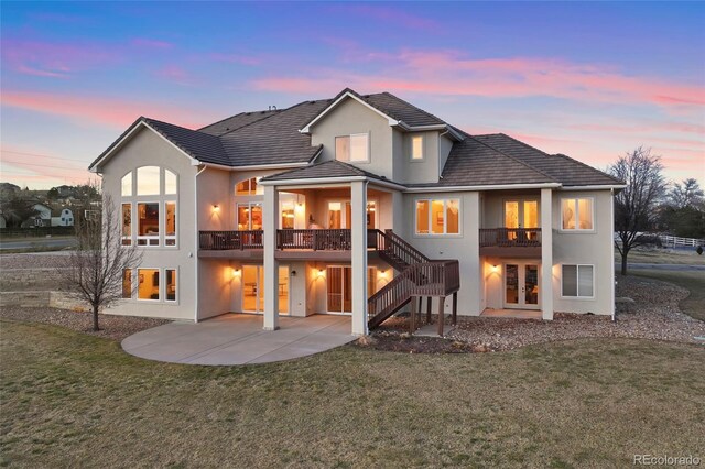 back of house at dusk featuring a lawn, a patio area, stucco siding, and french doors