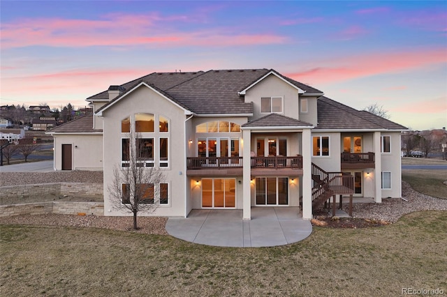 back of house at dusk with a yard, a patio area, stairs, and stucco siding