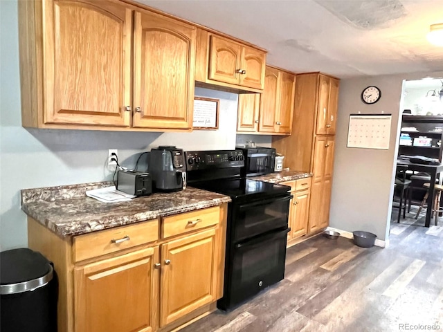 kitchen with dark hardwood / wood-style flooring, dark stone counters, and black appliances