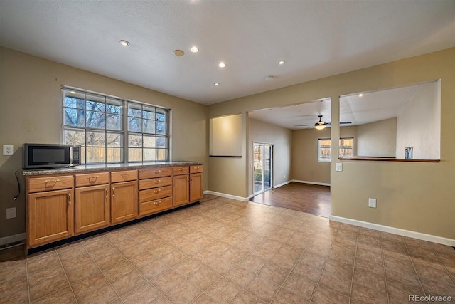 kitchen featuring baseboards, ceiling fan, dark stone countertops, recessed lighting, and brown cabinets