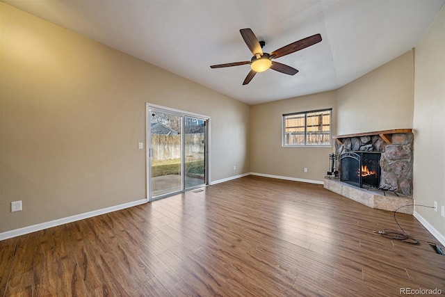 unfurnished living room featuring wood finished floors, baseboards, lofted ceiling, ceiling fan, and a stone fireplace