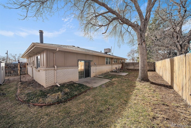 rear view of property featuring brick siding, board and batten siding, a lawn, a fenced backyard, and a patio area