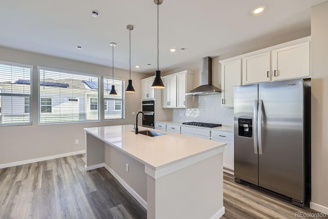 kitchen with white cabinetry, a center island with sink, gas cooktop, stainless steel fridge, and wall chimney range hood