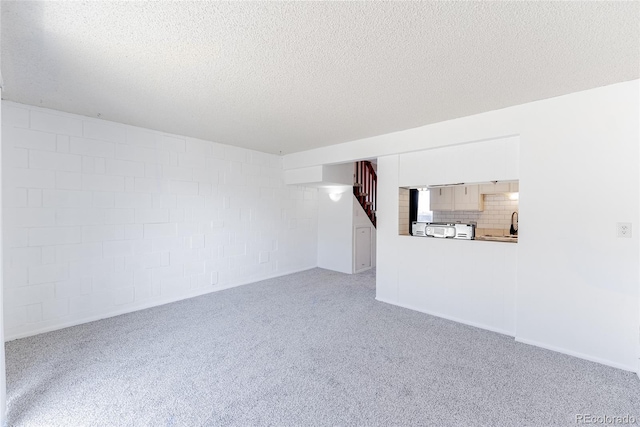 unfurnished living room featuring stairway, a textured ceiling, and carpet flooring